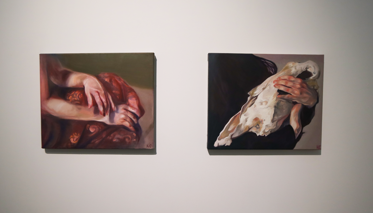 two paintings of hands, one is draped delicately over cloth; the other is caressing a bleached animal skull