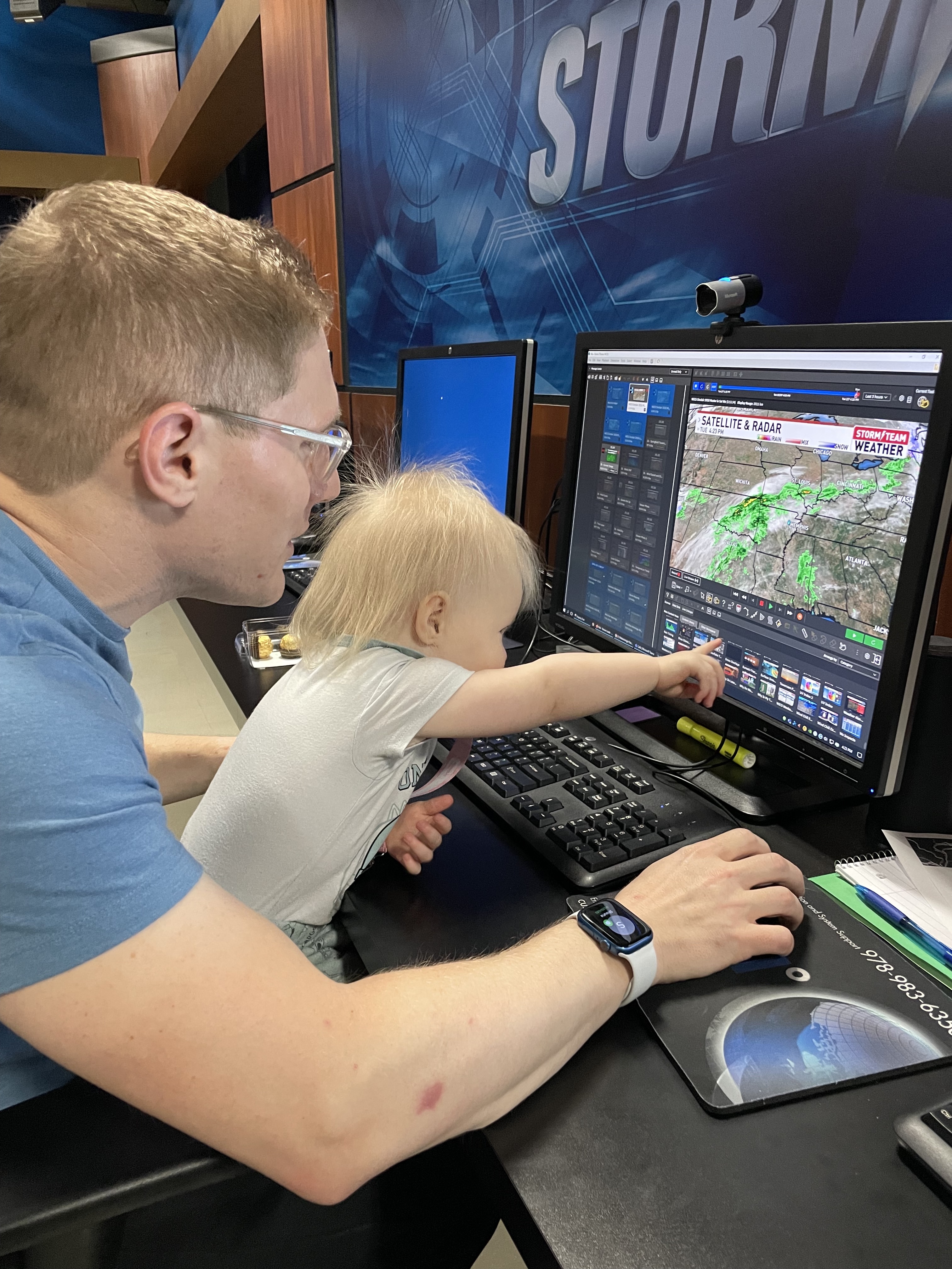 Former “SkyWatch” Forecaster, Darren Leeds (’11), shows his daughter, age 2, the graphics for his show at WCCU in Champaign, Illinois. Photo used with Permission.