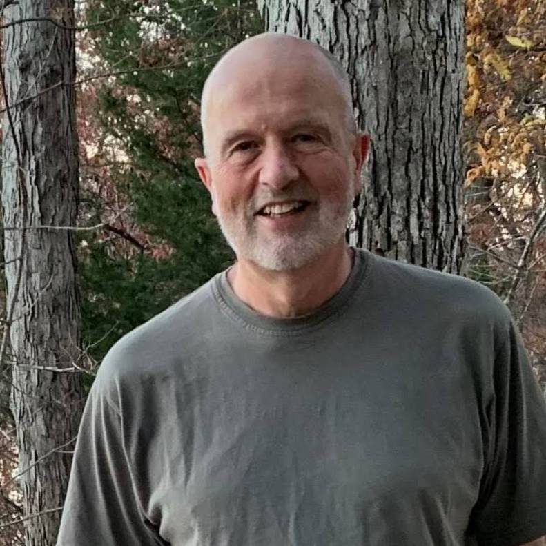 man standing in woods in jeans and tee