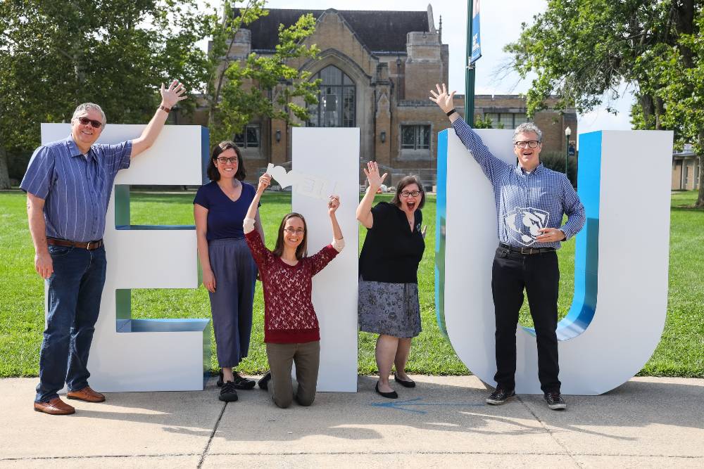 Librarians from the Research Engagement and Scholarship unit posing in front of the library's north entrance with  6-foot tall EIU letters.