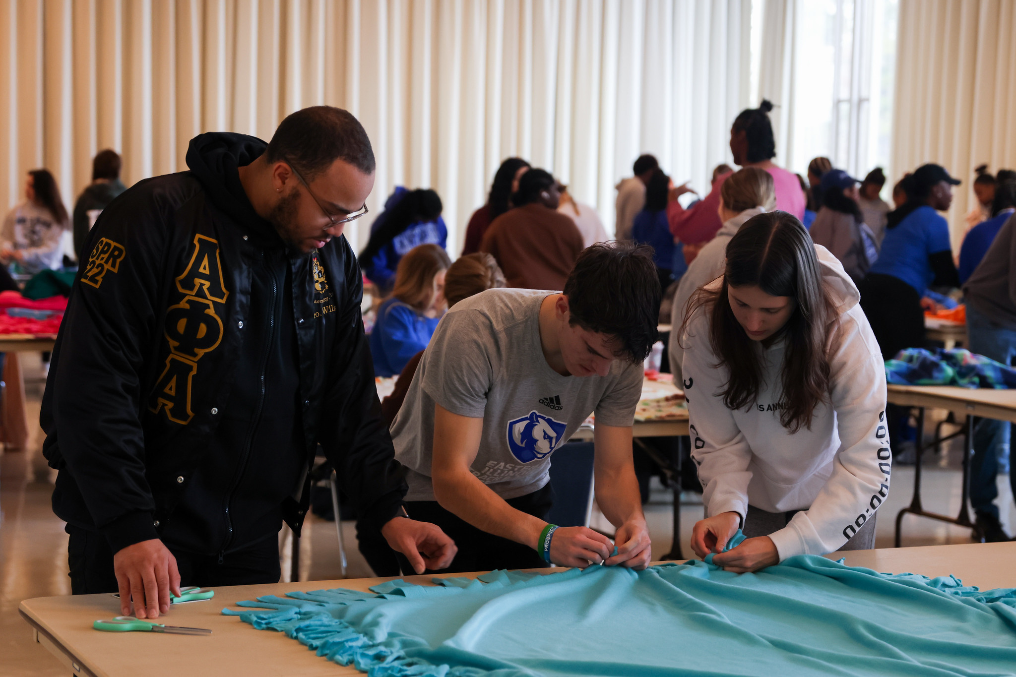 Three students working on constructing a fleece blanket