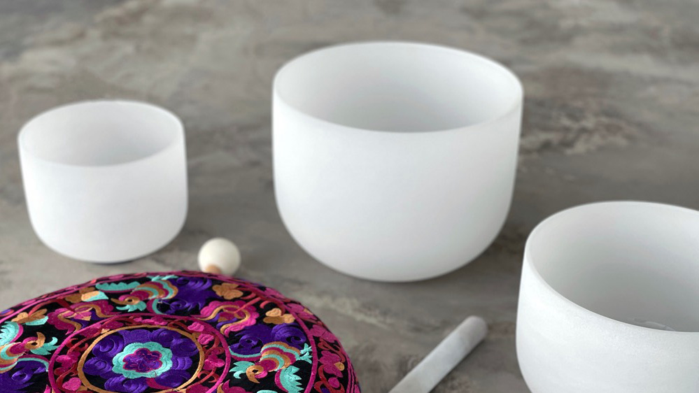 Three crystal bowls surrounding a round, multicolored cushion and two mallets.