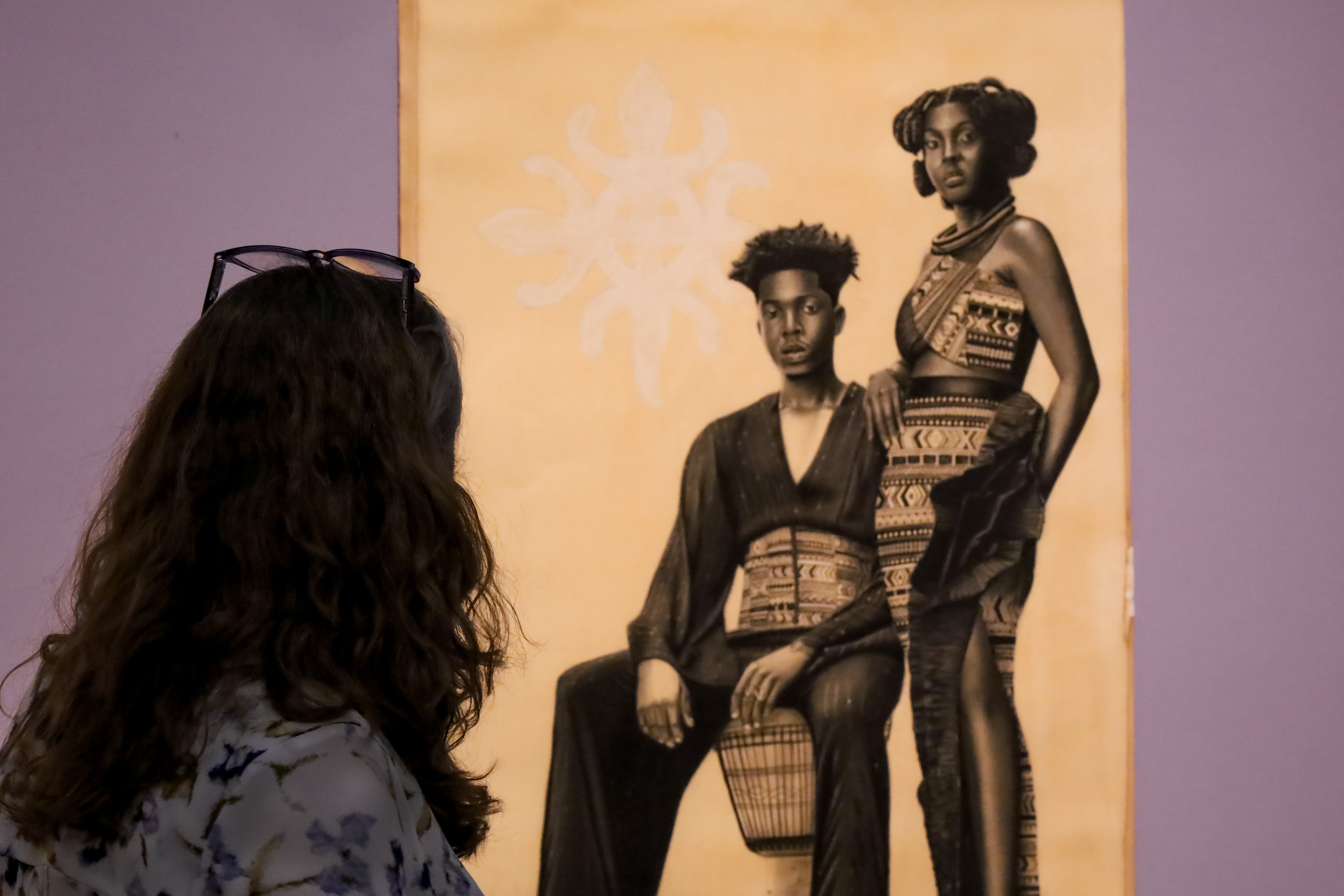 A woman, seen from the back, looks at a work of art on yellowed paper showing two figures in African inspired dress