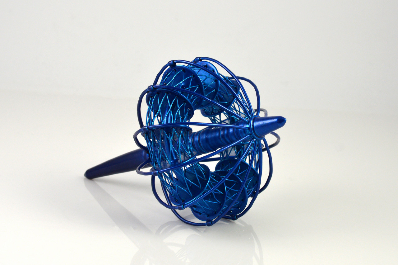 A metallic blue spindly top sits on a white platform on a white backgound.
