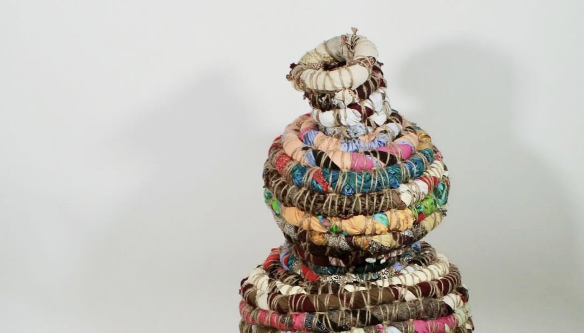 A vase-shaped woven artwork sits in the middle of the frame. It is made large coils of colored fabric
