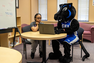 Billy Panther, school mascot, with student in writing center at table. 